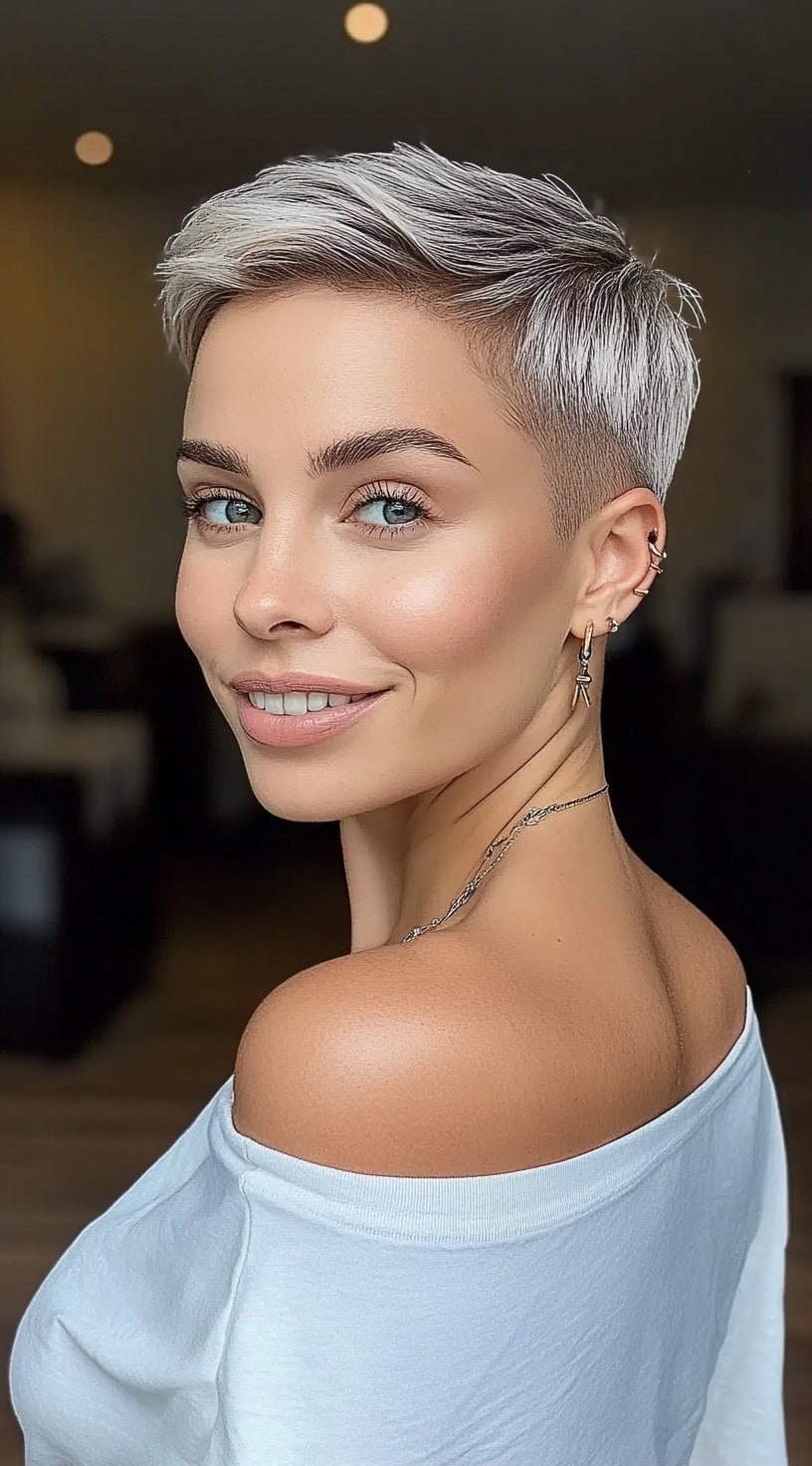 Женщина с морозно-серебристой стрижкой пикси, объемной на макушке и зауженными боками, улыбается через плечо.