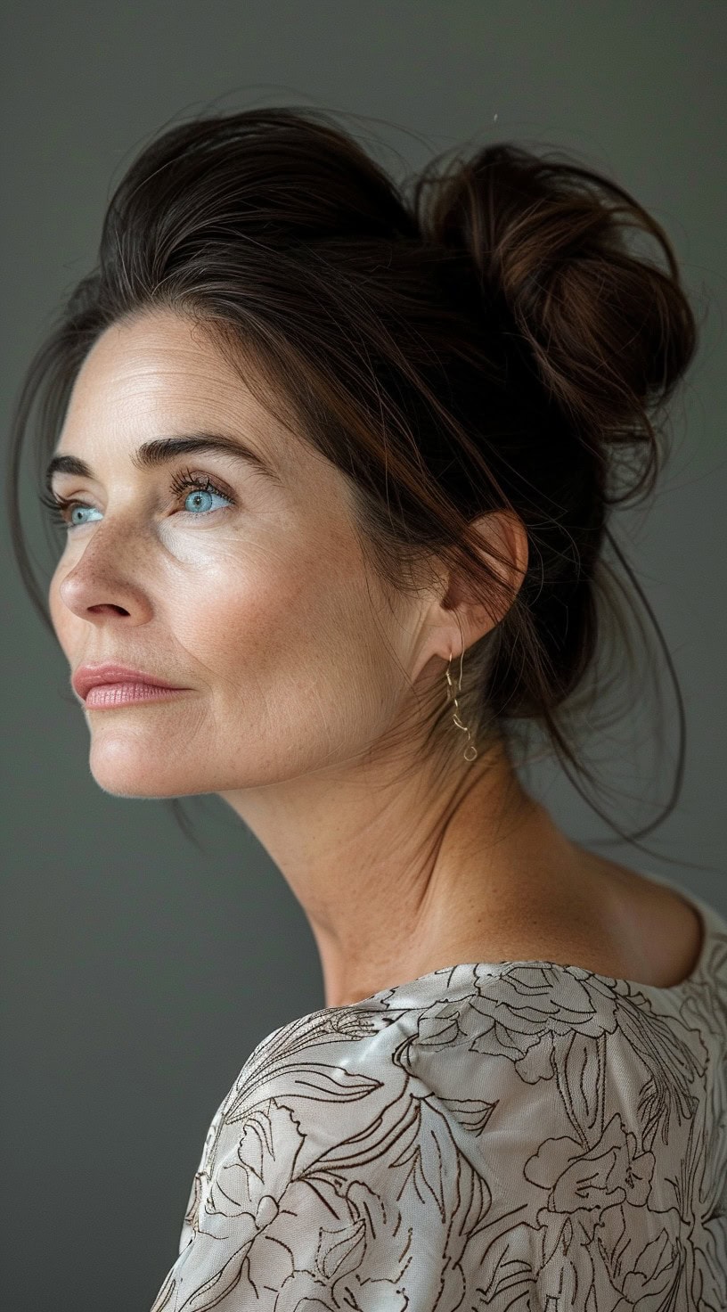 A messy high bun on a woman with dark brown hair styled loosely, with a few strands framing her face.